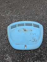 Front view of light blue Volkswagen Beetle rear deck lid showing ventilation slots, handle area with rust, and faint writing marks.