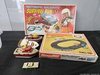 Vintage Motorific Racerific Survival Run XL set box with racing driver and car illustration, plus three boats and one small car on black surface.