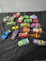 Top down view of all 15+ Tootsie Toy vehicles arranged on black surface showing various cars, trucks, and trailers in assorted colors and conditions.