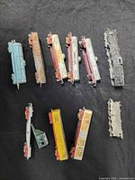 Overhead view of nine cast metal toy trains laid out on a cloth background showing varied colors and paint wear.