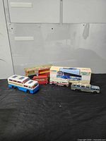 Five toy buses arranged on black surface against a white background, showing overall collection including boxed and loose models