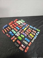 Overview photo showing approximately 40 colorful vintage Tootsie Toy cars laid out on a black surface, arranged in rows to show different models and colors.