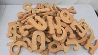 Pile of over 50 raw wooden letters and numbers for crafting, showing natural wood grain and smooth edges.