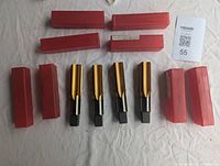 Four identical new metal taps with gold-colored threads and black square drive ends, each accompanied by a red box on a white surface.