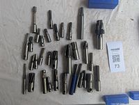 Top view of assorted milling cutters arranged on a white cloth, approximately 27 metal cutters of varying sizes and types.