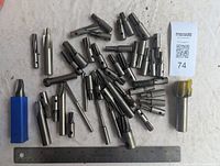 Photo of assorted milling cutters spread out with a ruler for scale showing approximately 6-inch length cutters, some in plastic case or with coated ends.