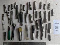 Full view of assorted milling cutters laid out, showing quantity and variety, some with colored covering and different shaft sizes.