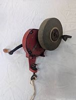 Front view of the hand cranked bench grinder showing red metal housing, grinding wheel and wooden handle.