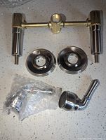 Metal valve body with two connecting posts and two round escutcheons, one lever handle wrapped in plastic nearby.