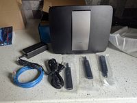 Linksys AC3200 router with power adapter, blue Ethernet cable, and three antennas.