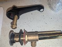 Matte black faucet spout and brass drain components shown assembled and unassembled on countertop.