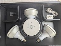 Top view of three Philips Hue smart bulbs arranged around a Philips Hue bridge with power adapter included in a black tray.