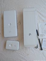 Three Ubiquiti networking devices on white sheet: two AirMax units and one smaller unit, with documentation and zip tie accessory.