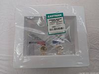 Front view of Eastman washing machine outlet box in packaging showing brand label and water valve fittings.
