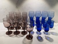 Lot arrangement showing 10 amethyst wine glasses, 4 blue wine glasses, and 10 blue liquor glasses in a group.