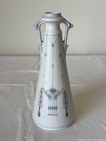 Front view of the tall porcelain vase with Art Nouveau handles and delicate hanging bead design displayed on tablecloth.