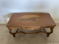 Front view of the carved wood coffee table showing ornate carved legs and stretcher base. The rectangular table top has a decorative edge and holds a custom glass surface.