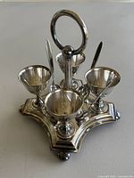 Front view of silver plated cruet stand with four egg cups and spoons inside