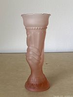 Front angled view showing single pink satin glass vase shaped as a hand holding a torch, flared top rim, and base with detailed designs.
