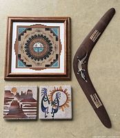 Lot overview with framed sand art, two sandcarved tiles, and boomerang all shown together on neutral background.