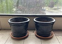 Two black glazed planters on matching saucers, front view.