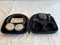 Headphones, travel case, charger, and cable displayed open on a flat surface.