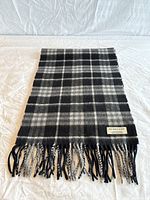 Front view of scarf laid flat showing full black and grey plaid pattern, fringe, and label