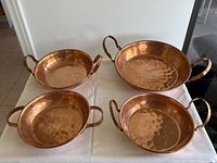 Set of four vintage copper pans with handles placed on a white cloth, showing all pans from above.