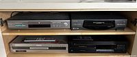 Front view of four electronic components arranged in a shelf: Samsung DVD player and Toshiba VCR on top, Sony DVD recorder and Nakamichi 7 Disc CD player below.