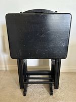 Front view of four black wood folding TV trays standing on their black wooden stand with a handle on the stand's top.