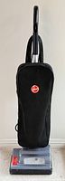 Front view of a black Hoover upright vacuum cleaner with a cloth bag and handle.