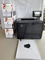 HP LaserJet Pro 400 M401dn black and white laser printer with three toner cartridges stacked and user manual on table.