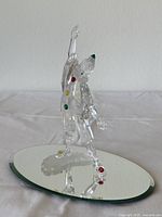 Full side view of the Pierrot figurine showing clear crystal construction, colored crystal accents on the costume, and the mirrored base underneath.