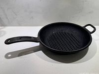 Top and angled view of the black cast iron grill pan showing the interior with raised ridges and handle with hole for hanging.