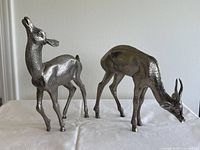 Pair of metal deer figurines side by side on white cloth background