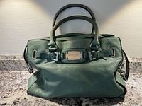 Front view of green textured leather Michael Kors handbag showing double handles, metal nameplate, and leather texture.