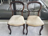Pair of vintage balloon back wooden chairs side by side showing condition and upholstery.