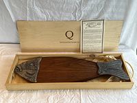 Wooden box containing the fish shaped serving platter with black walnut wood body and pewter decorations, includes informational paper.