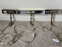 Three vintage brass picture lights with cords visible, all positioned on the floor against a wall.