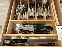 Top drawer containing organized cutlery and knives with handles in black and kitchen tools like peelers and peelers in a wooden organizer.