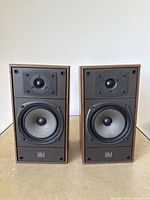 Front view showing pair of Celestion DL4 bookshelf speakers without grilles, featuring woofer and tweeter drivers and Celestion DL4 branding on speaker baffle.
