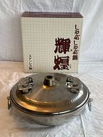 Front view of the stainless steel shabu-shabu hot pot with lid and original box in background