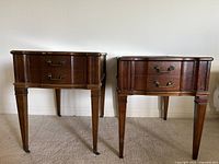 Front view of two vintage side tables, showing leather tops, wood finish, and single drawers with brass-tone pulls.