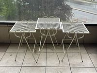 Three vintage off white metal stacking tables with square mesh tops and curved tubular legs, photographed from front and angled views to show stacking capability and design details.