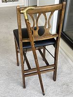 Walking cane leaning against a wooden chair showing entire length and handle.