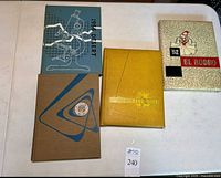 Four vintage hardcover yearbooks from 1952, 1953, 1956, and 1957 displayed on a table showing front covers and spines.
