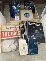 Entire lot with space memorabilia including bottles, coffee can, handbooks, record, magazines and newspapers displayed on floor.