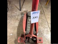 Front top view of red mechanical floor jack with visible lifting pad and gear mechanism, showing lot tag.