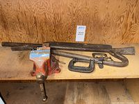 Overall view of bench vise, C-clamps and pry bars on wooden shelf