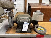 Front view of black Ohio Forge 6 inch bench grinder with 6 inch grinding and wire brush wheels, showing protective guard and worn condition.